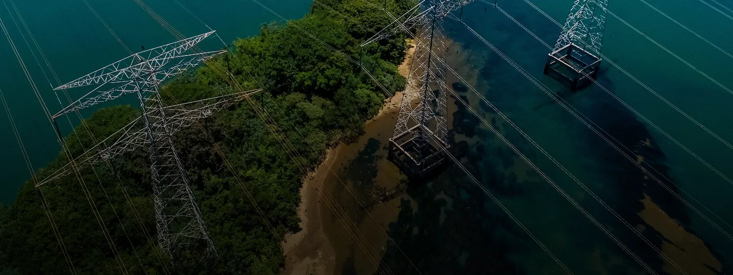 Vista aérea de torres e linhas de transmissão de energia junto à água e à vegetação