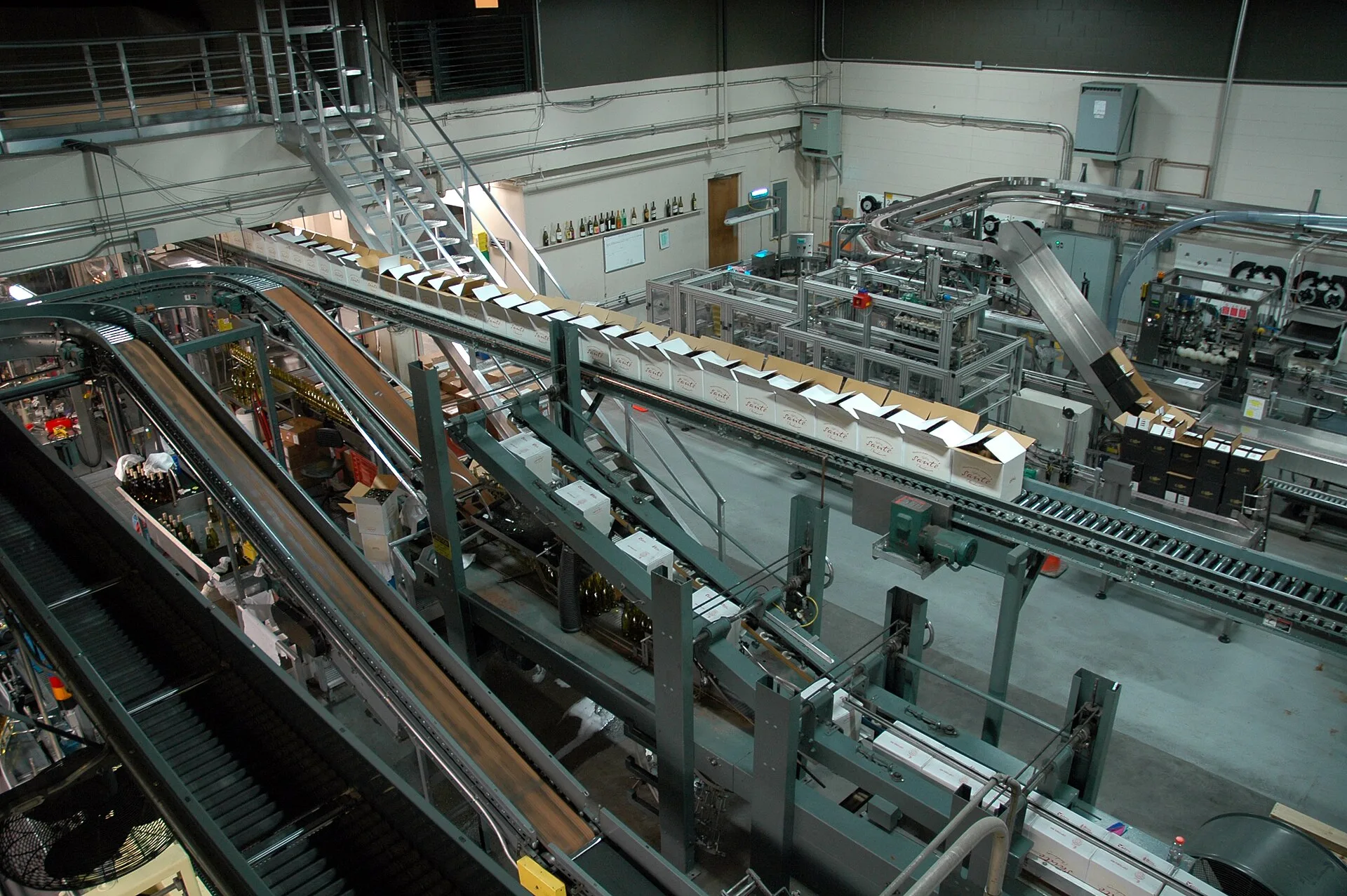 Linha industrial de engarrafamento e embalagem de bebidas, com esteiras e máquinas em um grande galpão