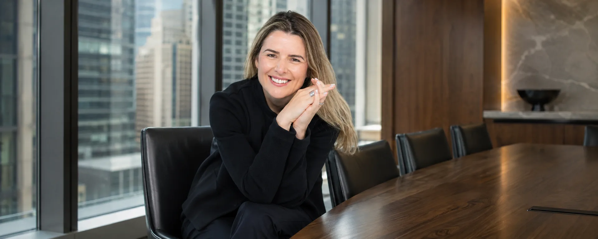 Andreza Araújo sorrindo, de roupa preta, em composição de escritório em Nova York