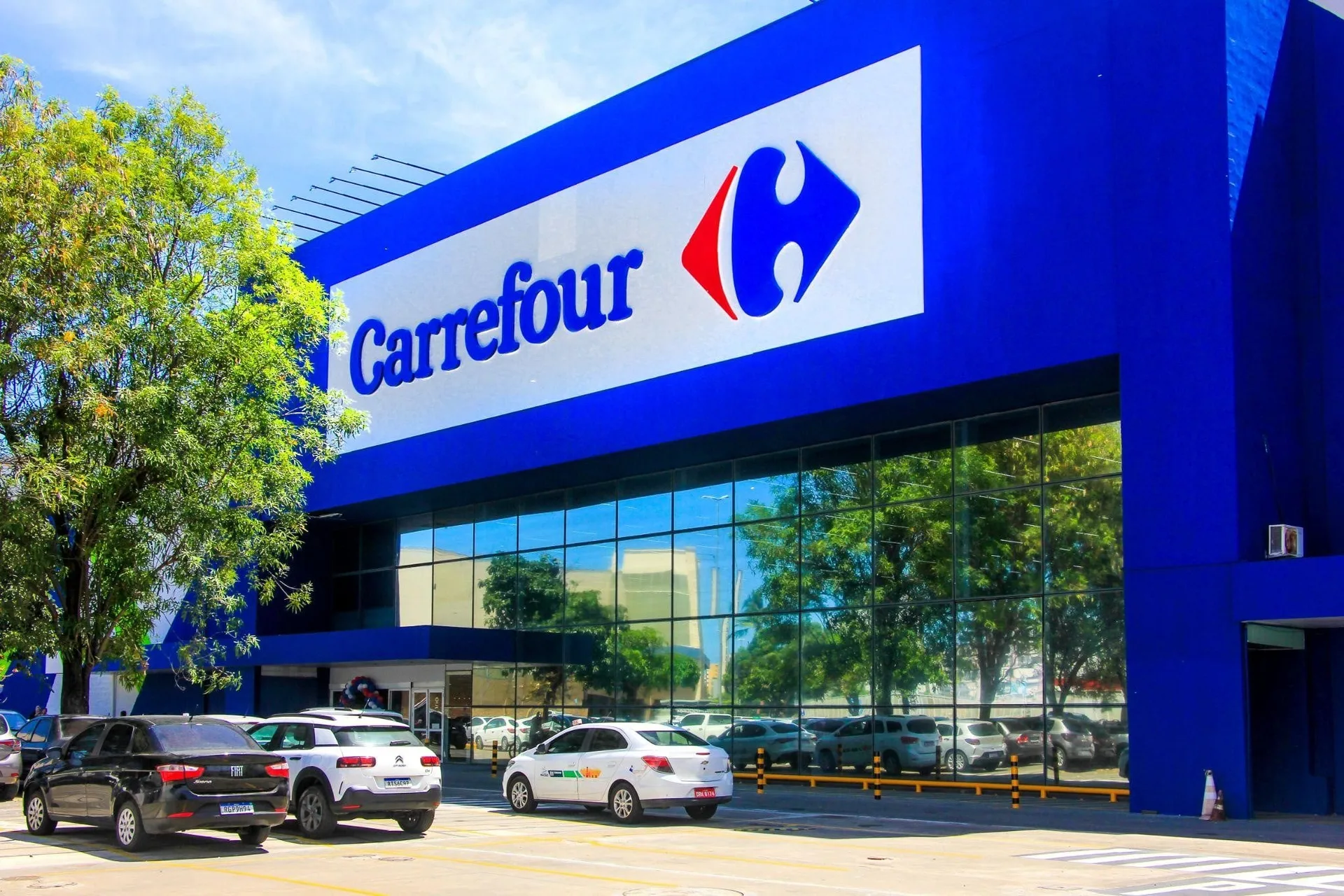Fachada azul de um hipermercado Carrefour no Brasil, com estacionamento e entrada de clientes