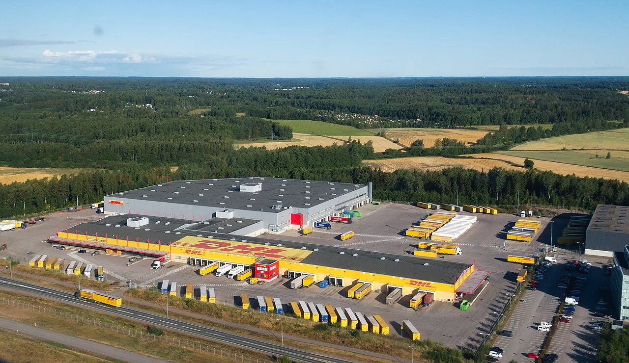 Vista aérea do centro logístico da DHL em Vantaa, Finlândia, com a marca no telhado e carretas nas docas
