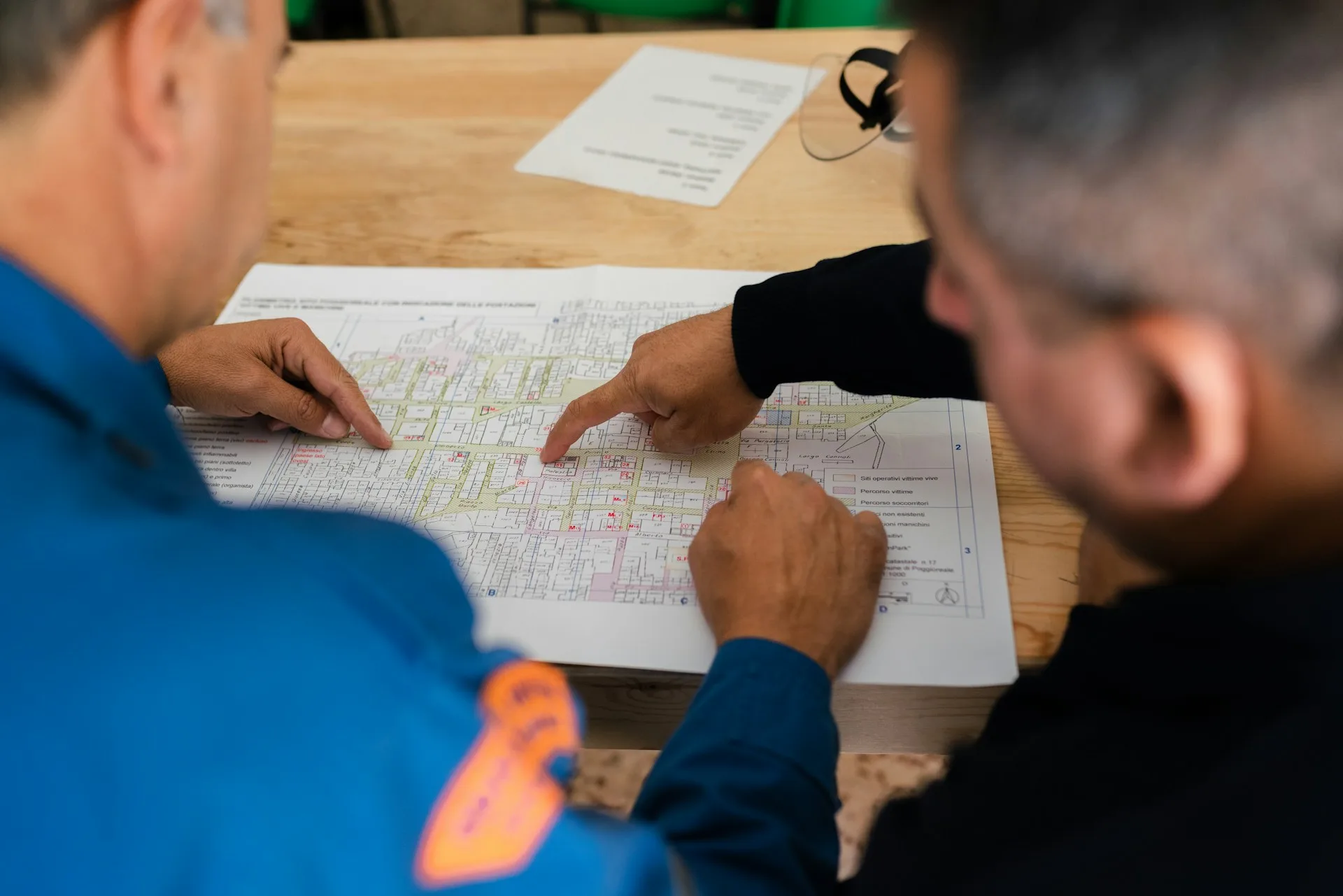Dois profissionais analisando e apontando informações em um mapa técnico sobre a mesa