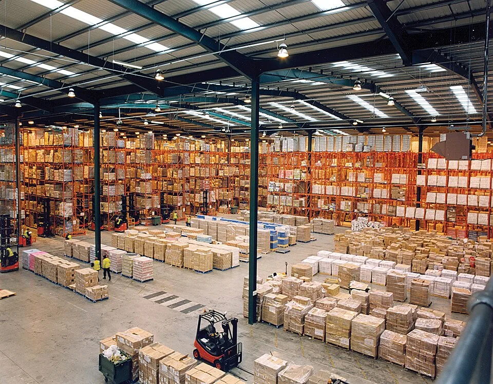 Interior de armazém com estruturas de armazenagem, cargas sobre pallets e empilhadeiras