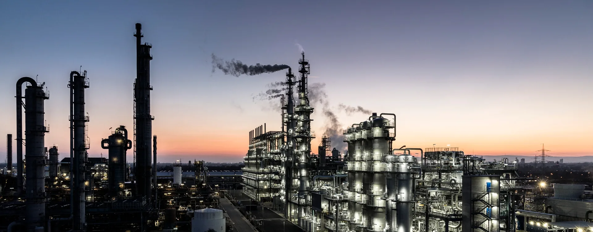 Torres e tubulações de uma planta química iluminadas ao entardecer